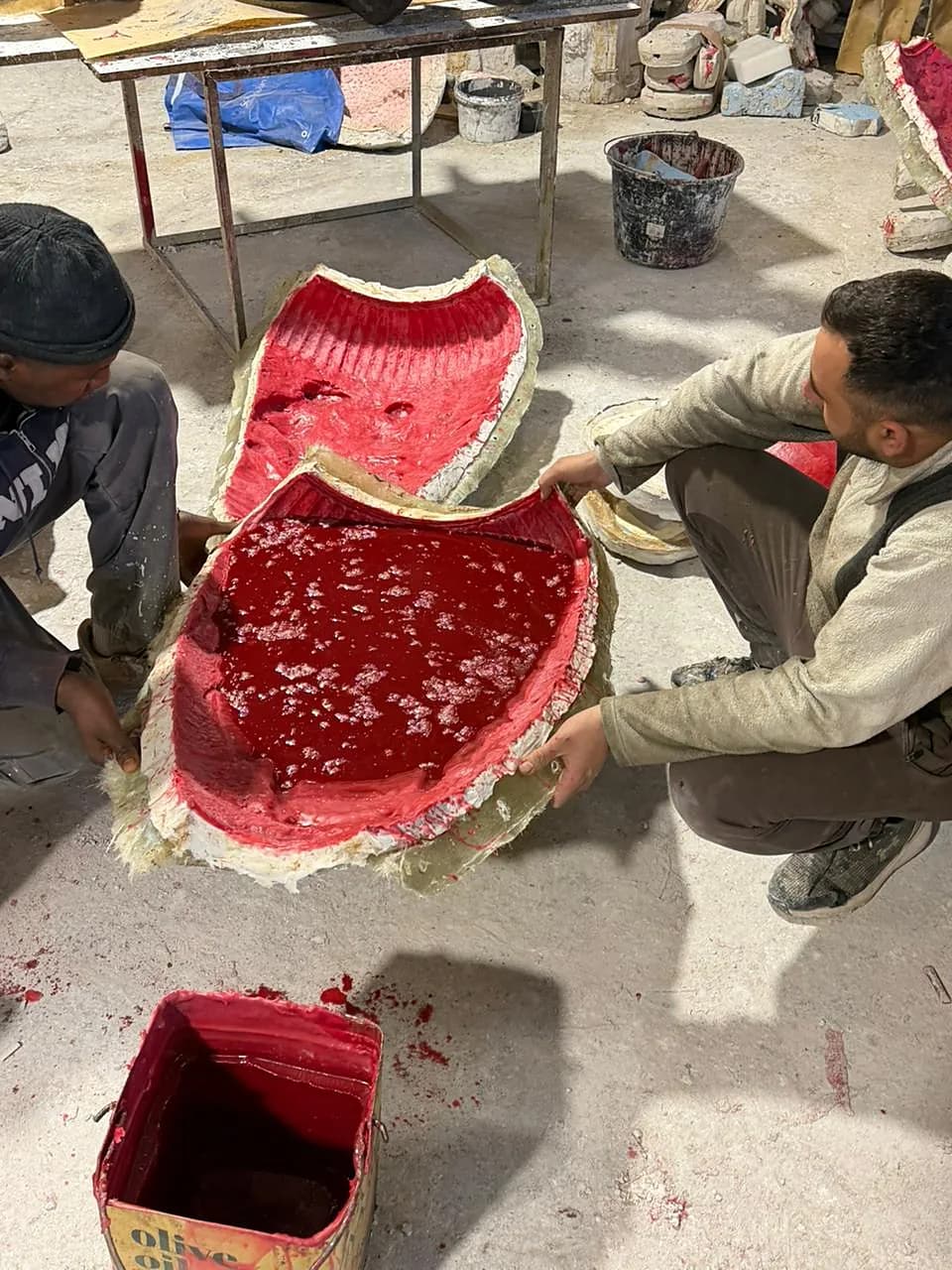 Two artisans lifting a red silicone mould from the form